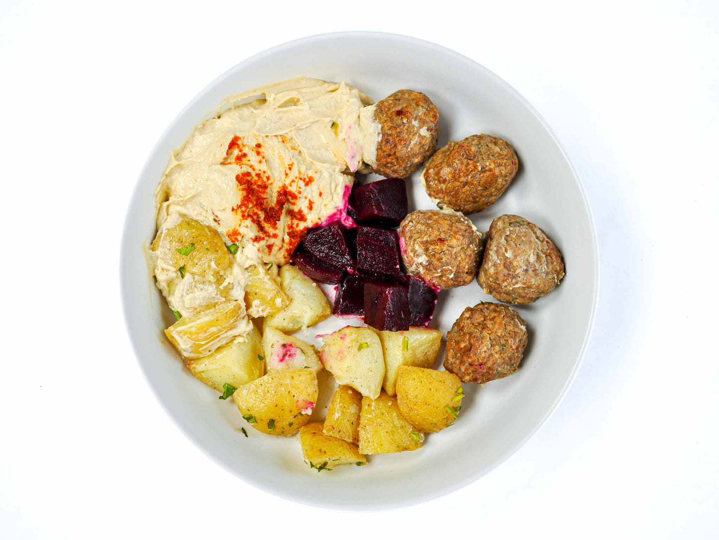 Sumac's Meatball Hummus Bowl features savory meatballs atop creamy hummus, complemented by roasted potatoes. This satisfying dish offers a delightful balance of flavors and textures, promising a hearty and wholesome meal at Sumac.