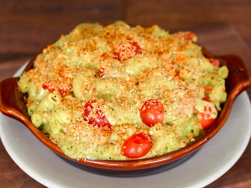 Homeroom's Garden Pesto Mac features a creamy blend of Gouda and Pecorino cheese, tossed with vibrant pesto and juicy cherry tomatoes. This comforting dish delivers a rich, herbaceous flavor with a fresh pop of sweetness, making it a delicious twist on classic mac and cheese.