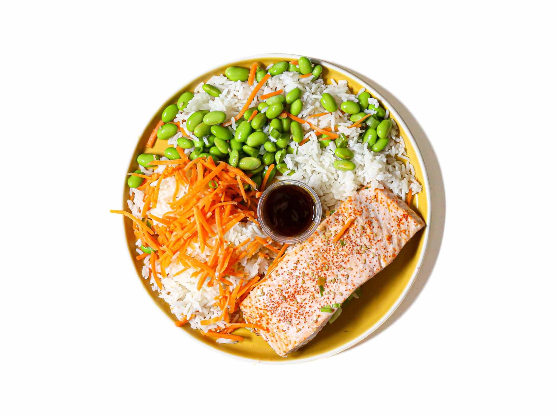 Buddha Bowl's  Teriyaki Glazed Salmon features tender, perfectly cooked salmon fillets brushed with a rich and savory teriyaki glaze. This is paired with white rice and steamed edamame beans. This dish offers a delightful balance of sweet and savory flavors, creating a delicious and satisfying meal.