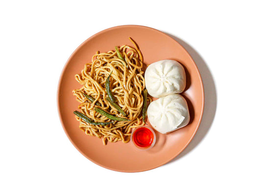 Koi Palace's BBQ Bao Box features fluffy bao buns filled with tender BBQ pork, paired with flavorful garlic noodles and hoisin-glazed green beans. This dish offers a perfect blend of sweet, savory, and tangy flavors, creating a satisfying and delicious meal.