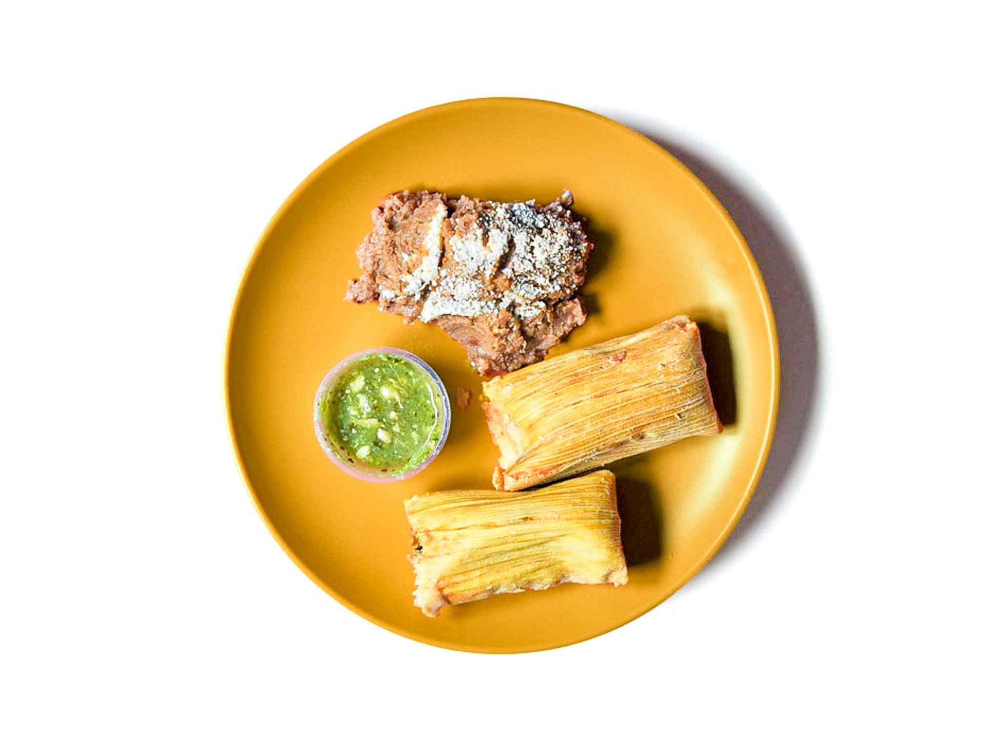 Burritos La Palma's Chicken and Green Chili Tamales feature tender chicken combined with vibrant green chili sauce, enveloped in a soft, flavorful masa. Paired with a side of creamy refried beans, this dish offers a perfect balance of spice and comfort in every bite.